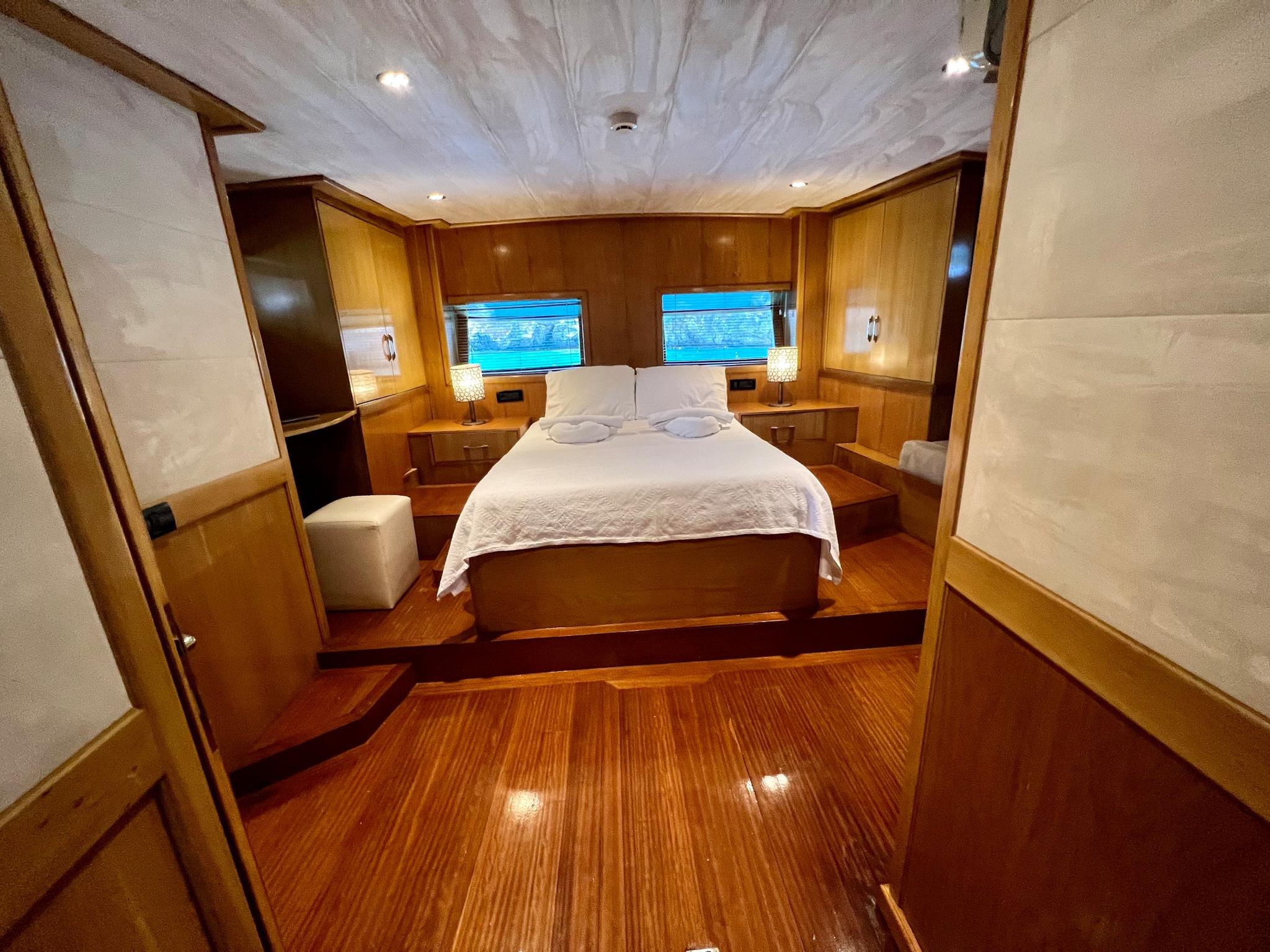 luxury yacht master cabin featuring double bed, wooden paneling, side portholes with ocean views
