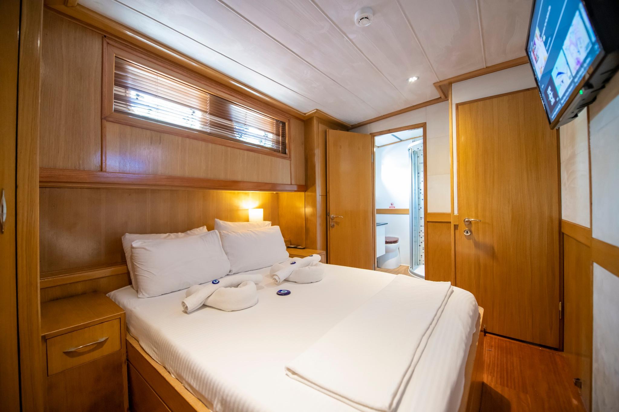 yacht guest cabin featuring double bed with white linens, wood paneling, porthole windows and ensuite bathroom access