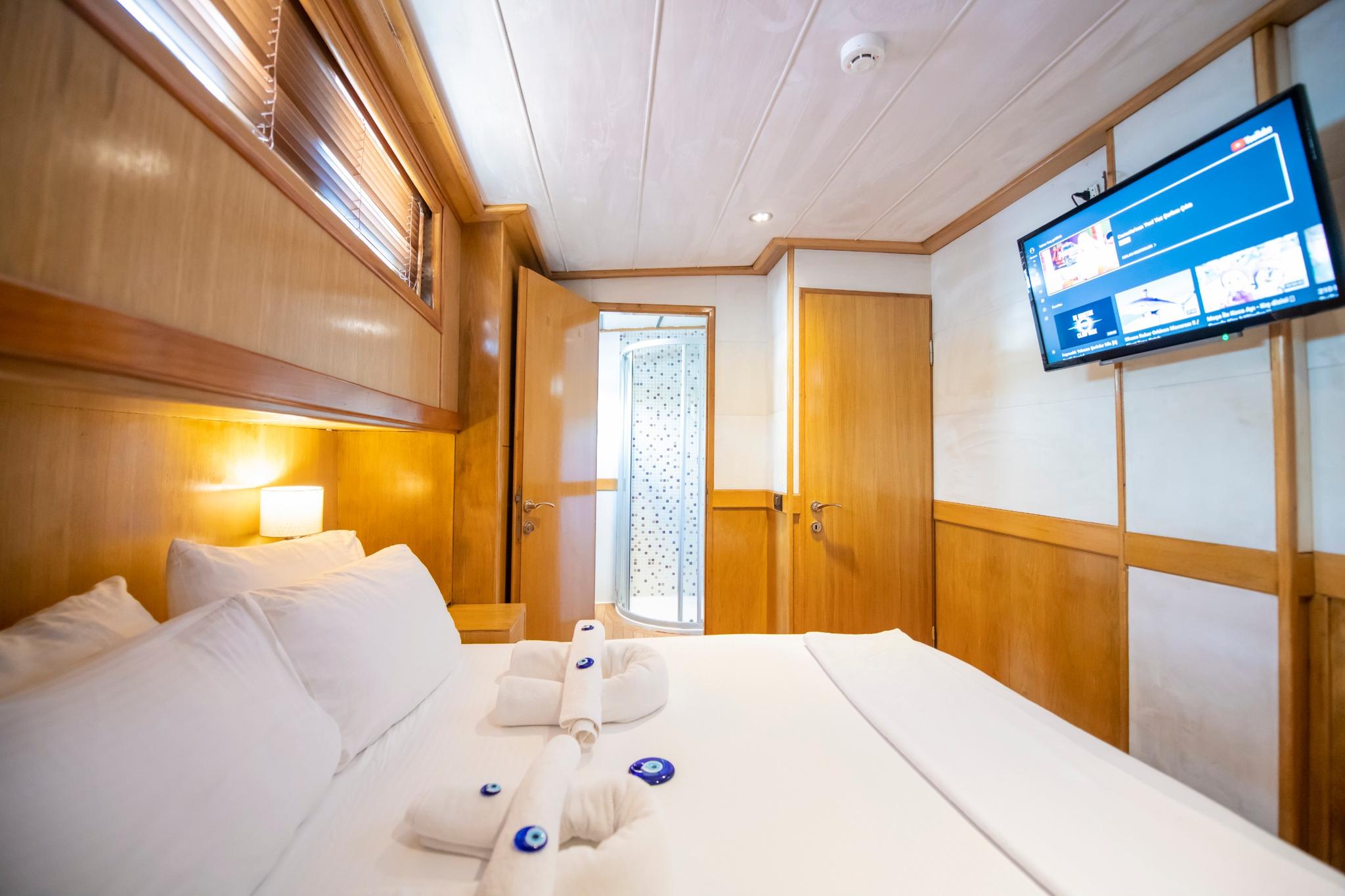 yacht guest cabin with white bedding, wooden paneling, wall-mounted television and en-suite door
