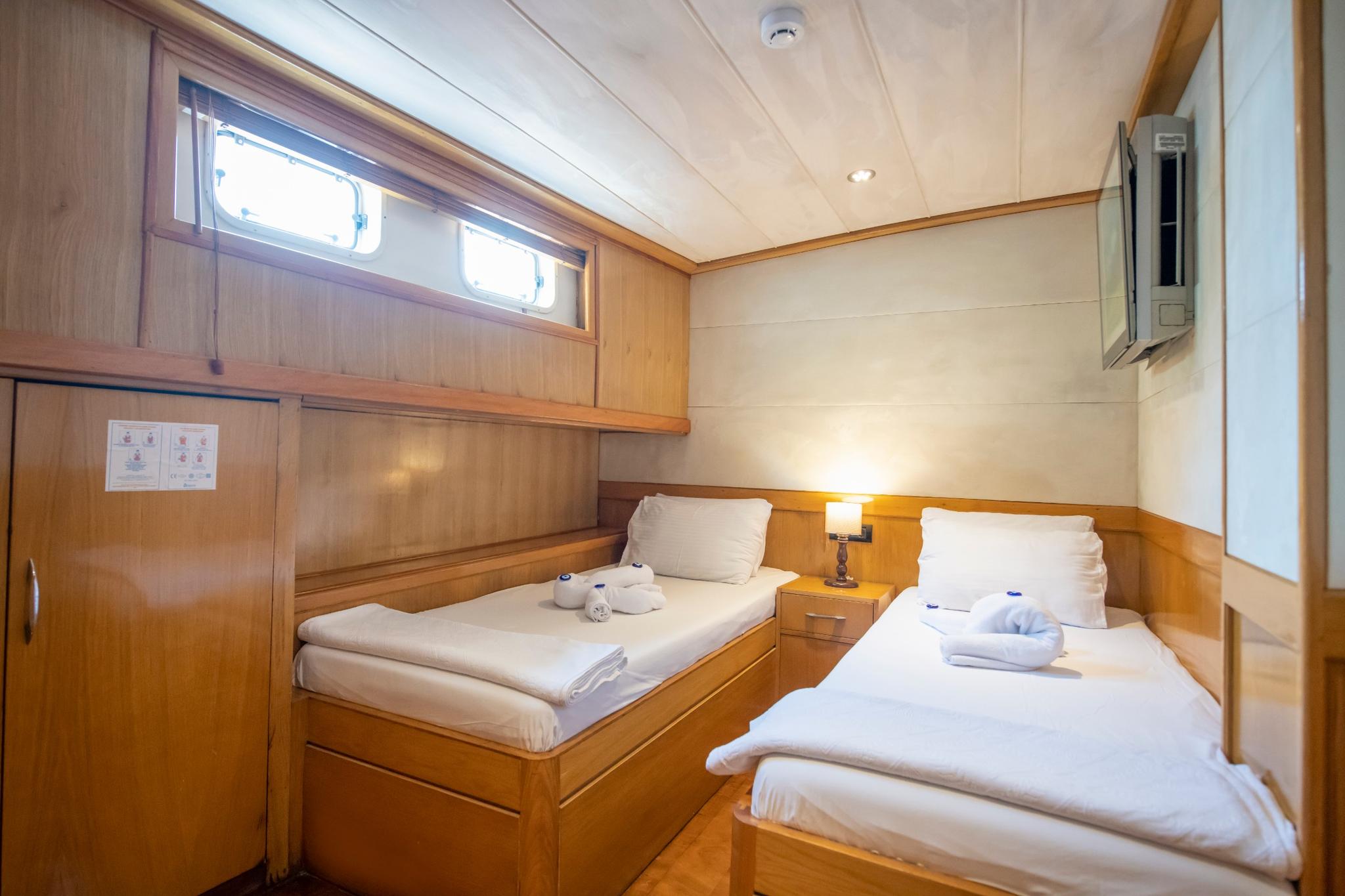 yacht twin cabin featuring two single beds with white linens, built-in storage drawers, and portholes
