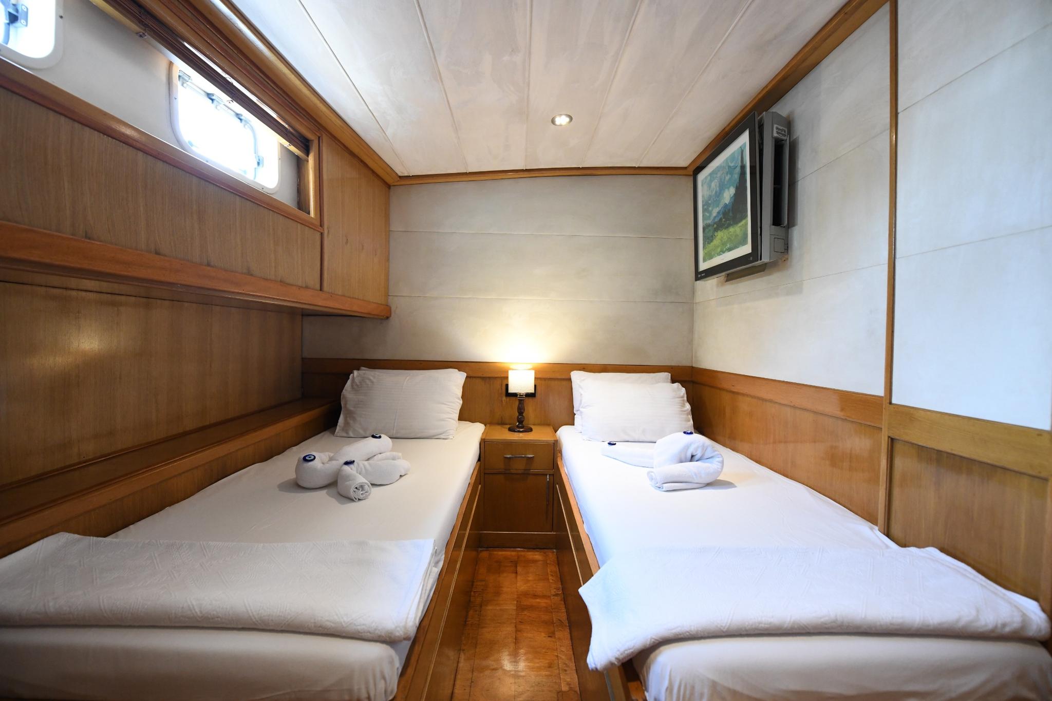 yacht twin cabin with two single beds, wooden nightstand, TV, and porthole windows