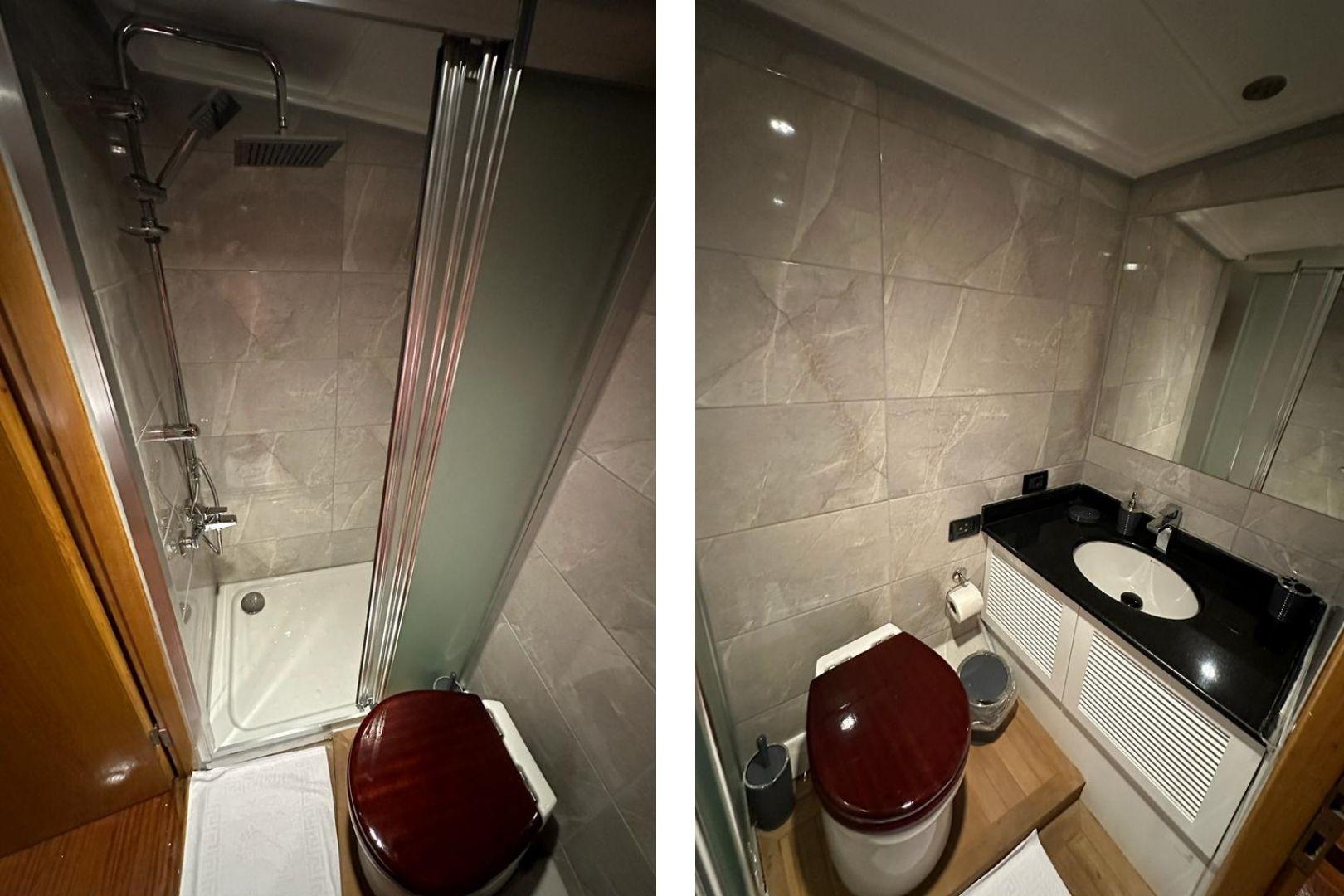 yacht bathroom featuring marble walls, glass shower enclosure, toilet with dark wooden seat and black granite vanity