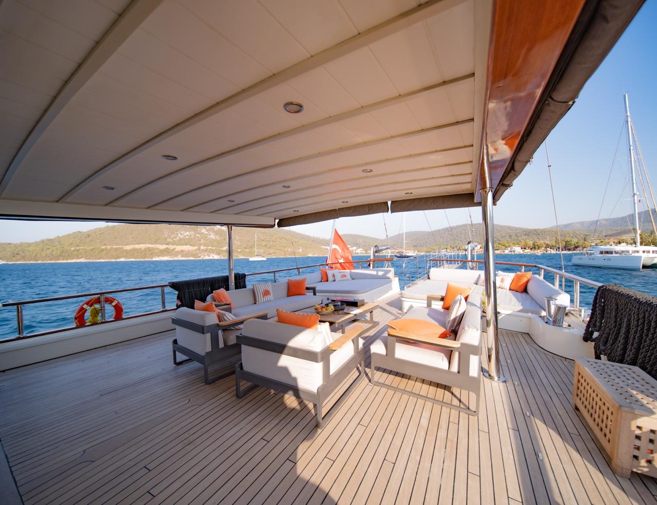 yacht aft deck with white sofas, orange cushions, teak decking under hardtop canopy