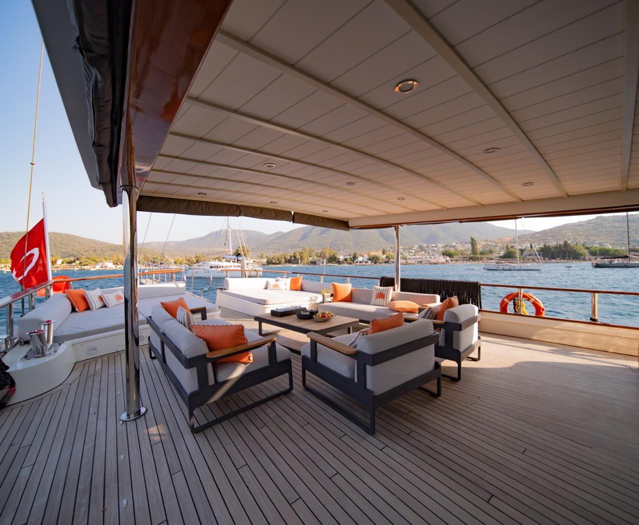 Aft deck lounge area with white sofas, orange cushions, coffee table under covered canopy