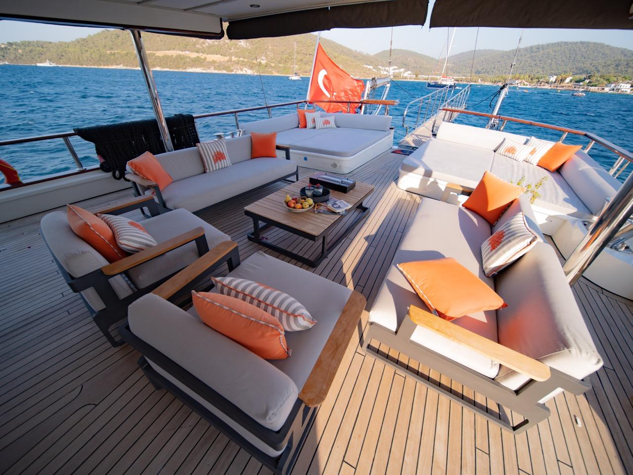 covered aft deck with white cushioned seating, orange pillows, and wooden coffee table