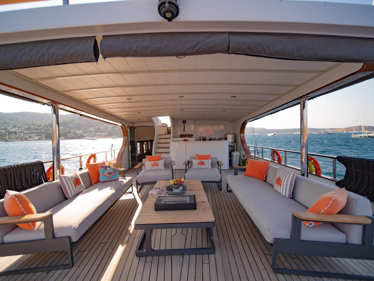 covered aft deck lounge with white cushioned seating, orange pillows, and galley kitchen