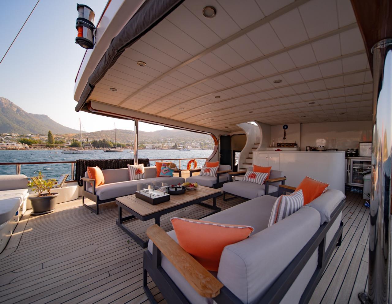 yacht aft deck lounge with white sofas, orange cushions, coffee table and galley