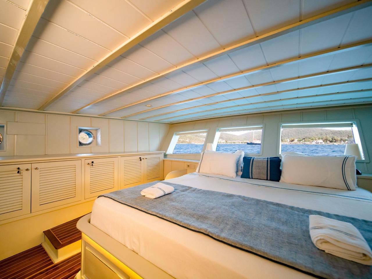 yacht cabin with double bed, white linens, built-in storage and panoramic side windows