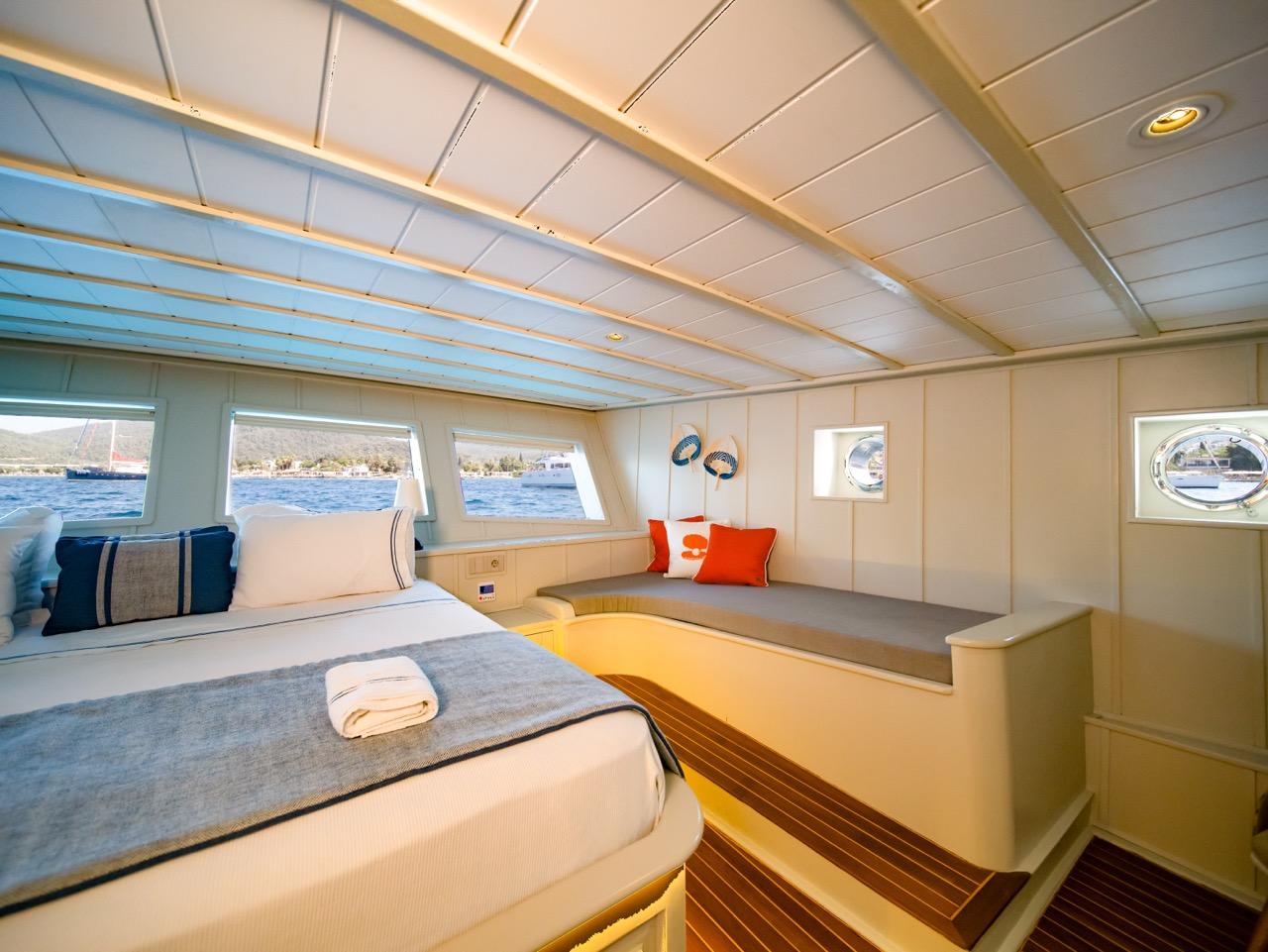 yacht cabin interior with double bed, built-in seating bench, panoramic windows and wooden flooring