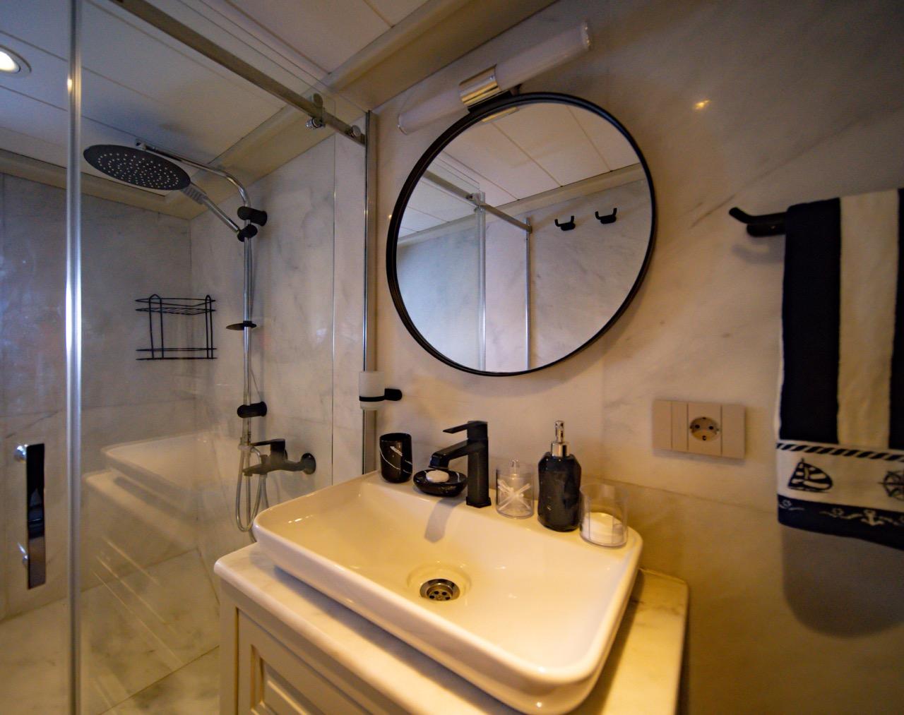 yacht bathroom featuring white ceramic sink, round black-framed mirror and glass shower enclosure
