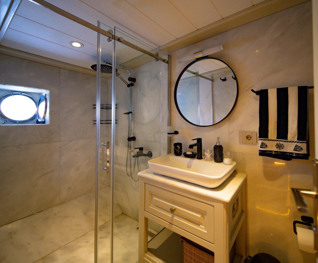 yacht bathroom featuring glass shower enclosure, white vanity with vessel sink and round mirror