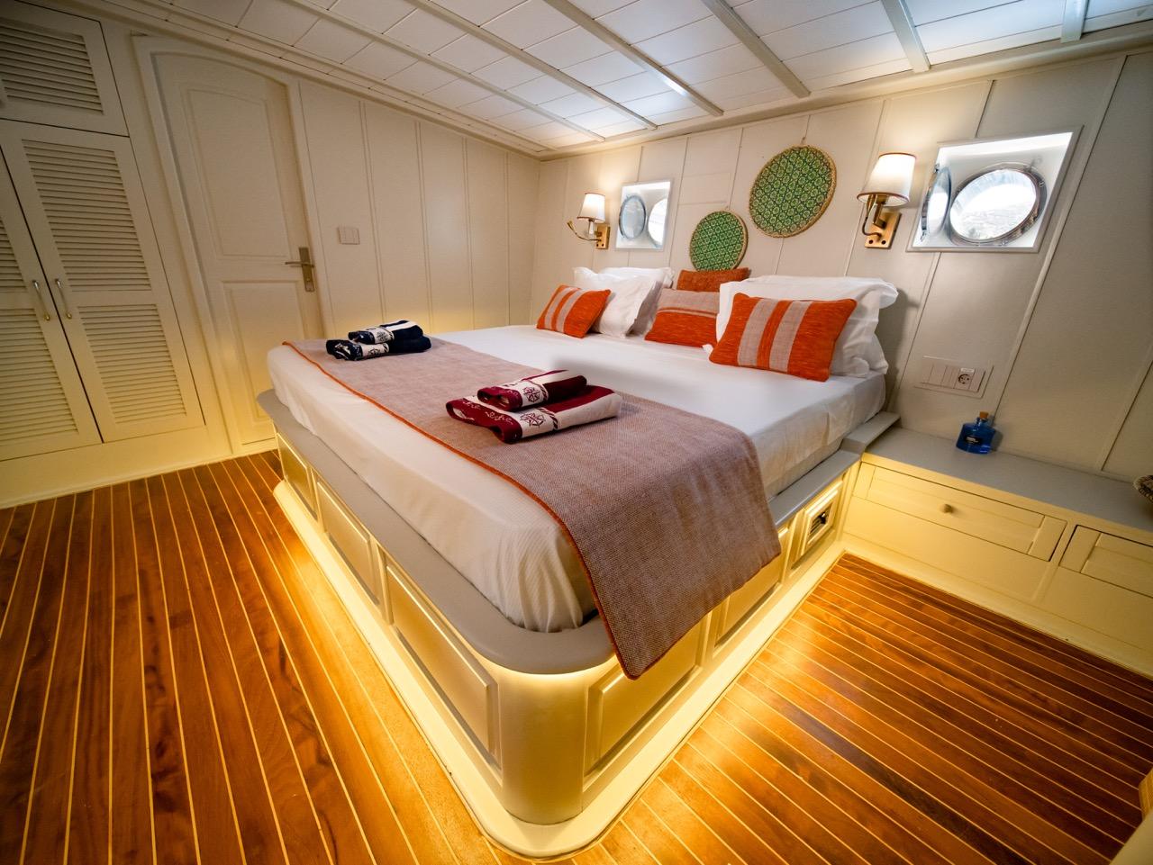 yacht guest cabin featuring white double bed with orange striped pillows and ambient LED lighting
