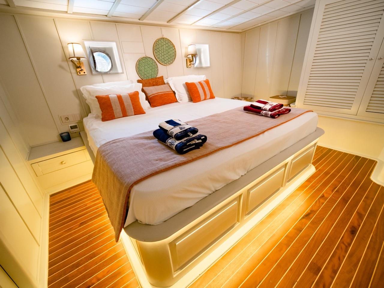 yacht guest cabin featuring double bed with orange striped pillows and white paneled walls