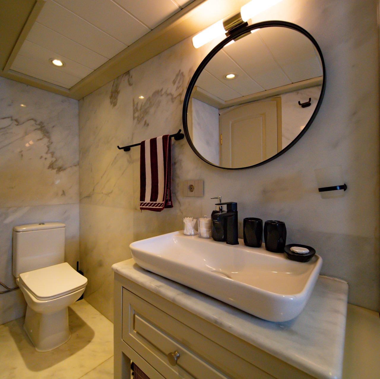 luxury yacht bathroom featuring white vessel sink, round mirror, marble walls and modern fixtures