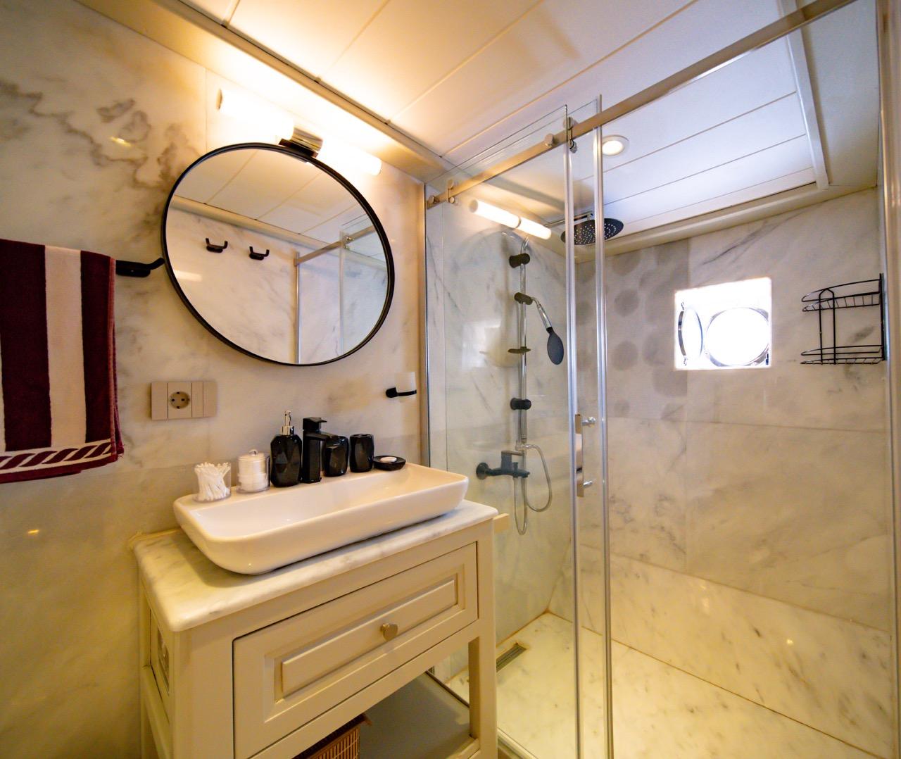 luxurious yacht bathroom featuring marble shower enclosure, vessel sink, and round mirror