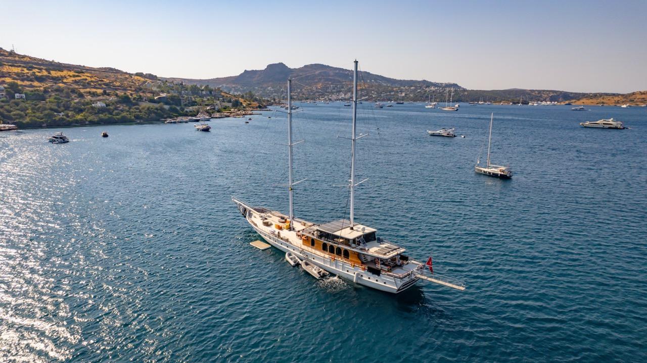 aerial view of traditional gulet yacht anchored in turquoise Mediterranean bay with mountainous coastline