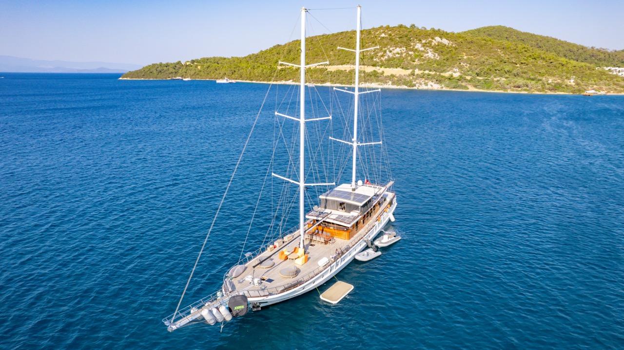 aerial view of white gulet yacht with two masts anchored in crystal clear turquoise waters near forested coastline