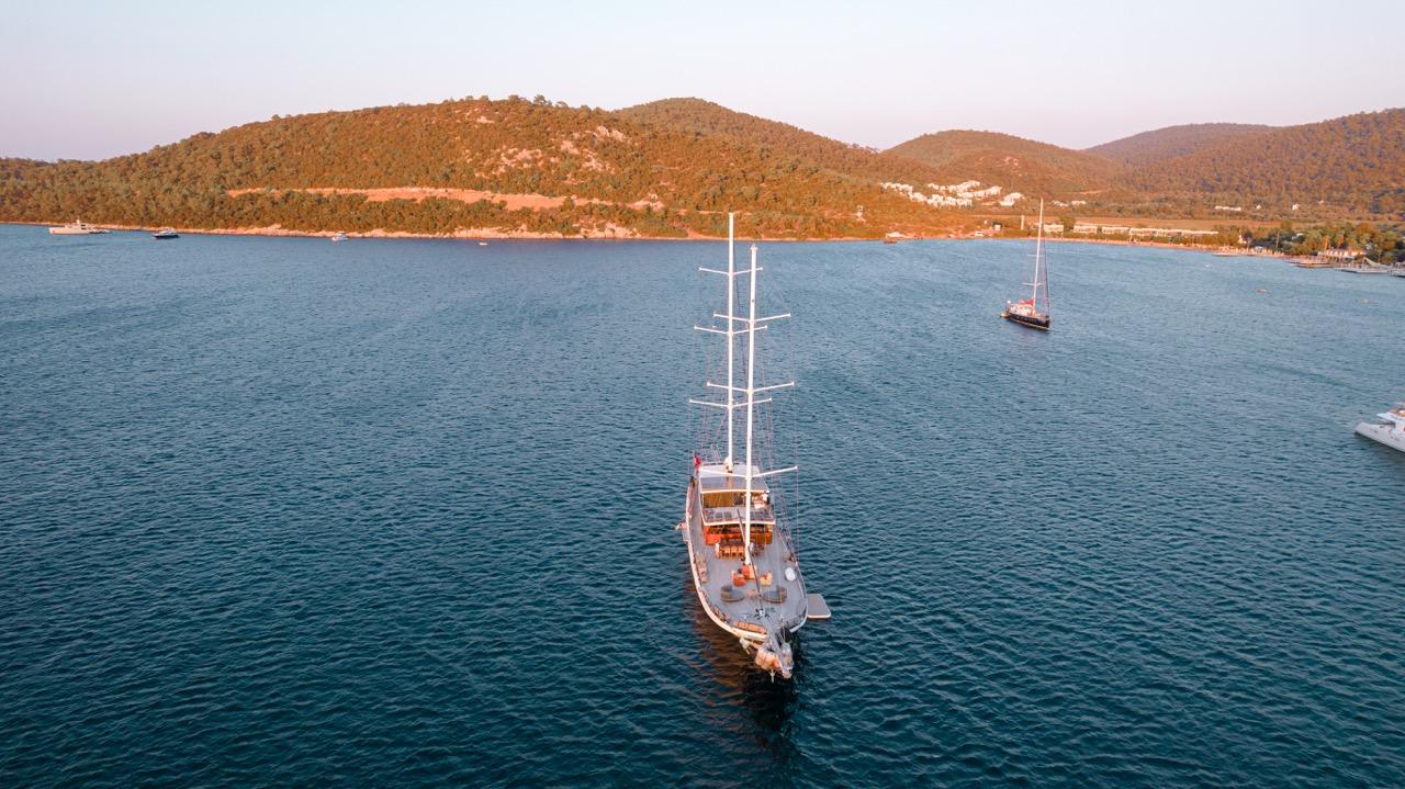 aerial drone shot of white sailing yacht with three masts anchored in turquoise Mediterranean bay