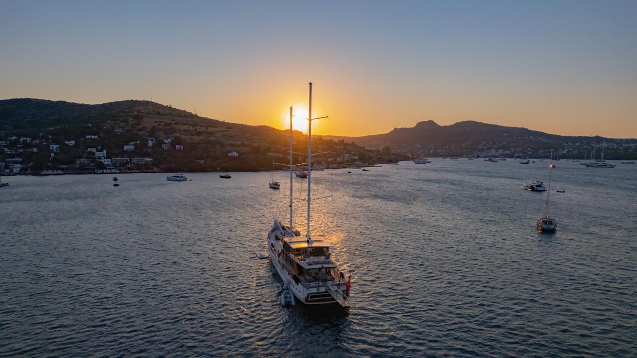 aerial drone shot of traditional wooden gulet anchored at sunset with golden sky and coastal hills