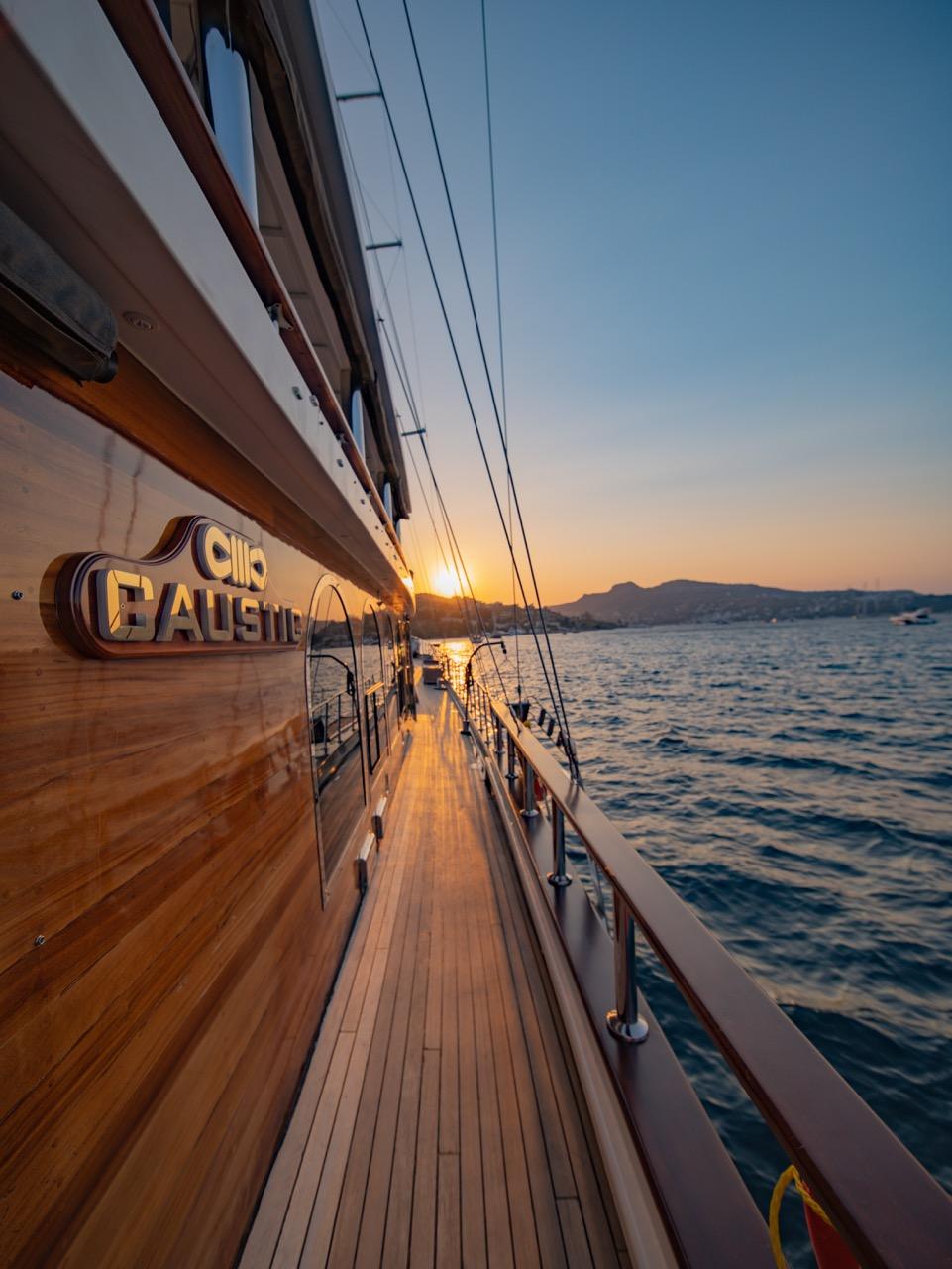 wooden side deck walkway of luxury yacht with teak decking and stainless steel railings at sunset
