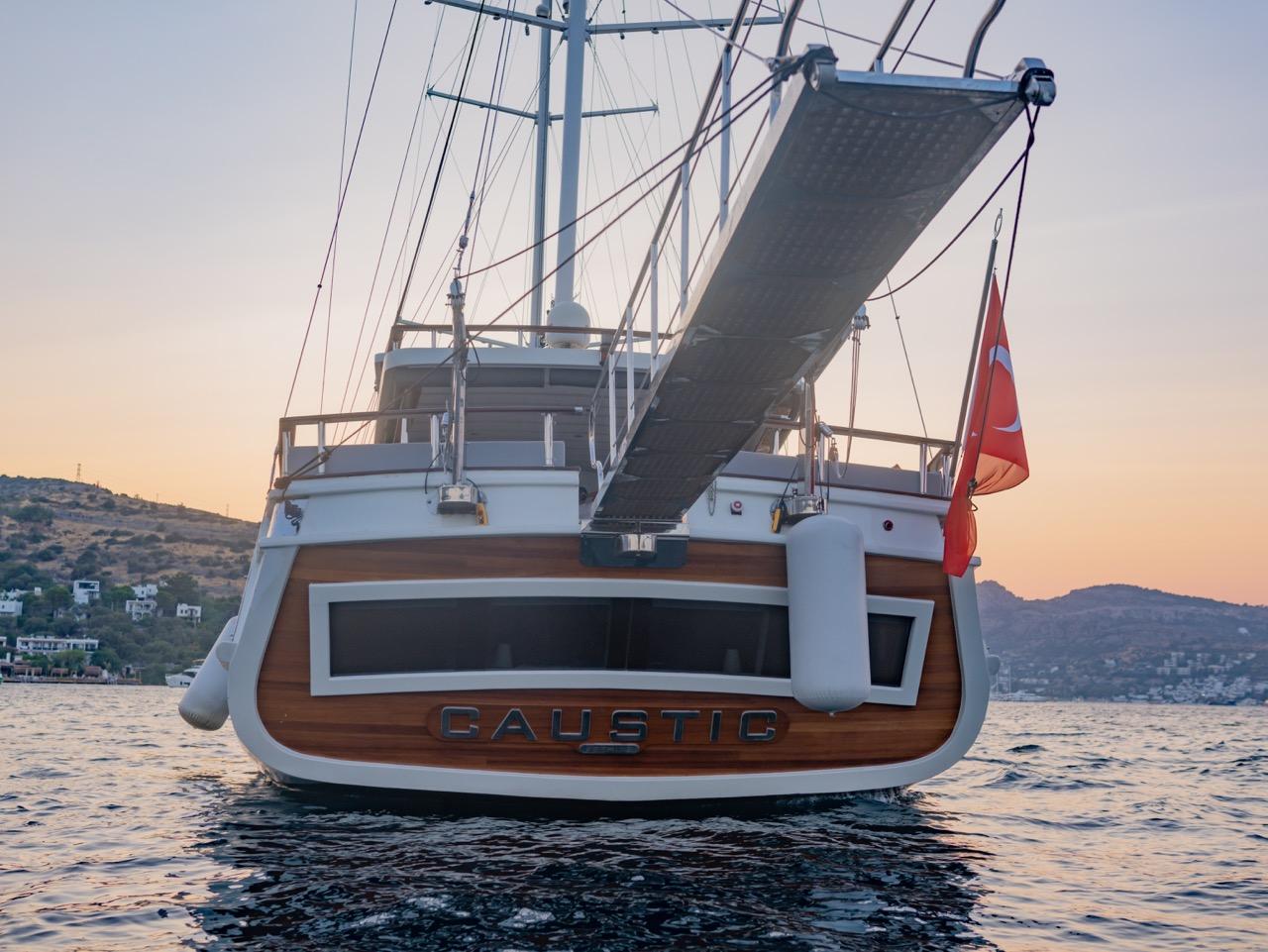 Caustic gulet stern view with wooden transom, sailing rigging and Turkish flag at sunset