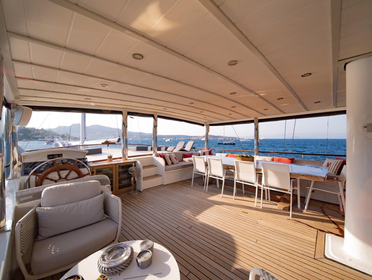 yacht aft deck with dining table, helm wheel, seating area and panoramic windows