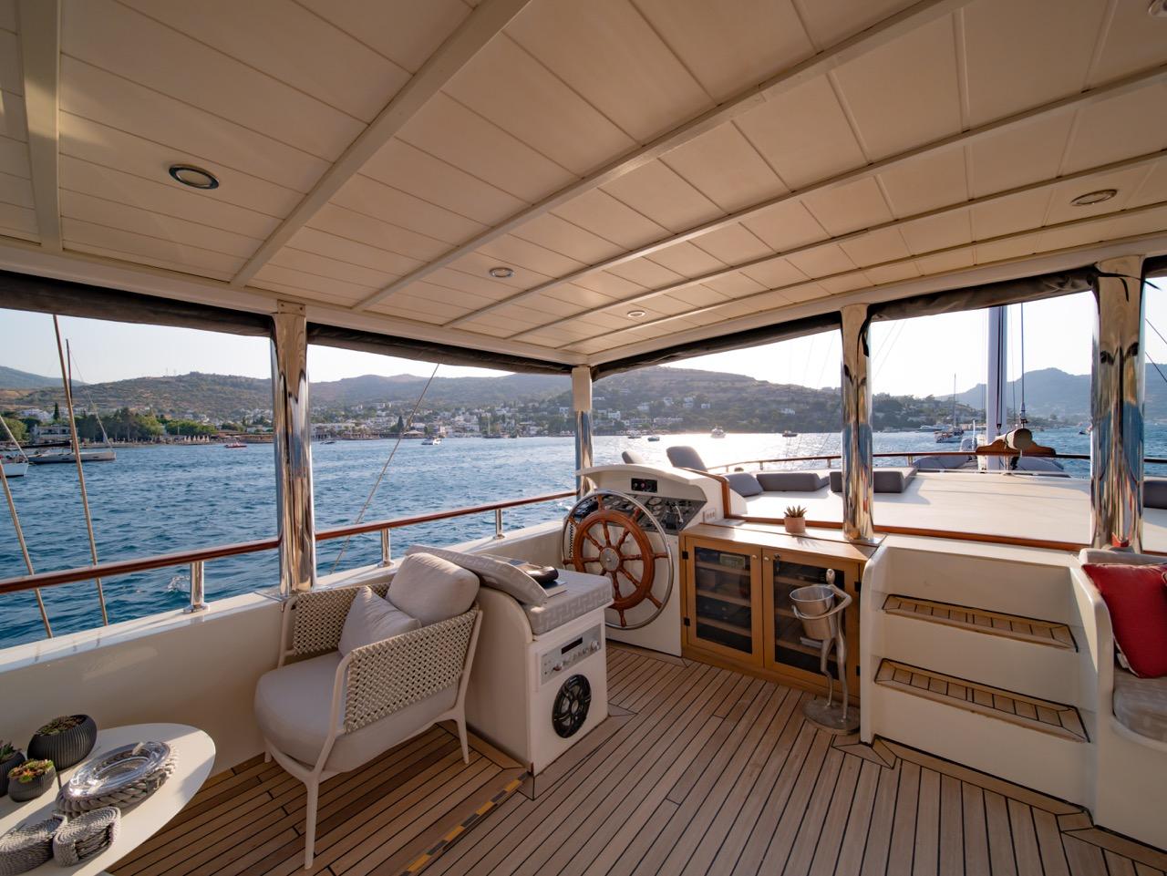 yacht wheelhouse deck with traditional wooden steering wheel, white seating and teak flooring
