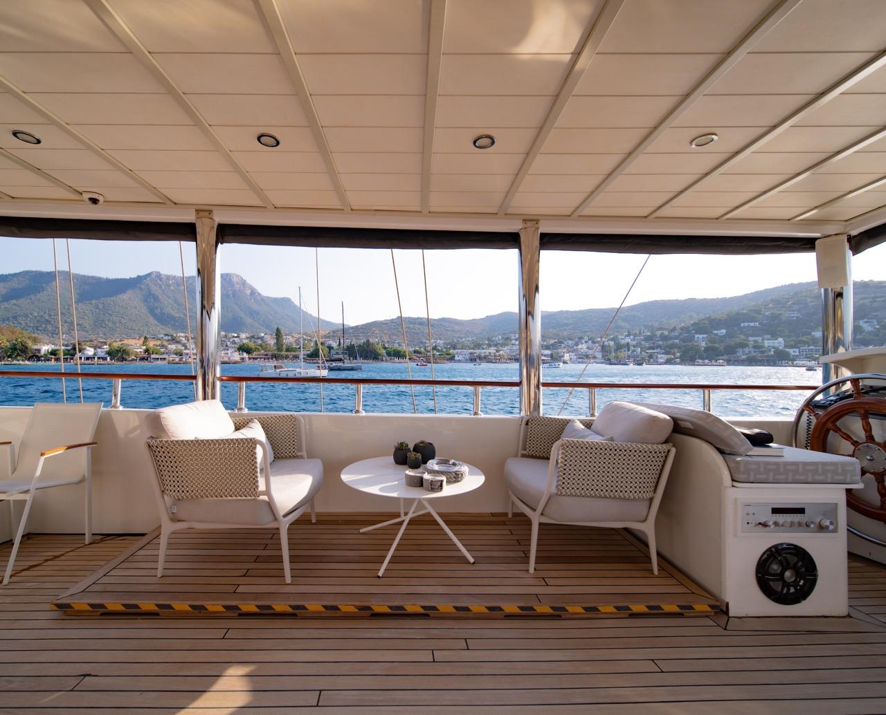 covered aft deck with white seating arrangement and panoramic windows overlooking coastline