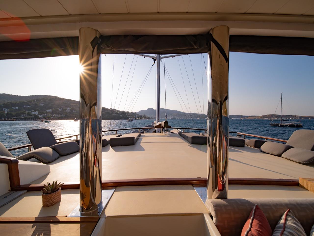 Gulet aft deck salon with white sofas and cushions overlooking Mediterranean coastline at sunset