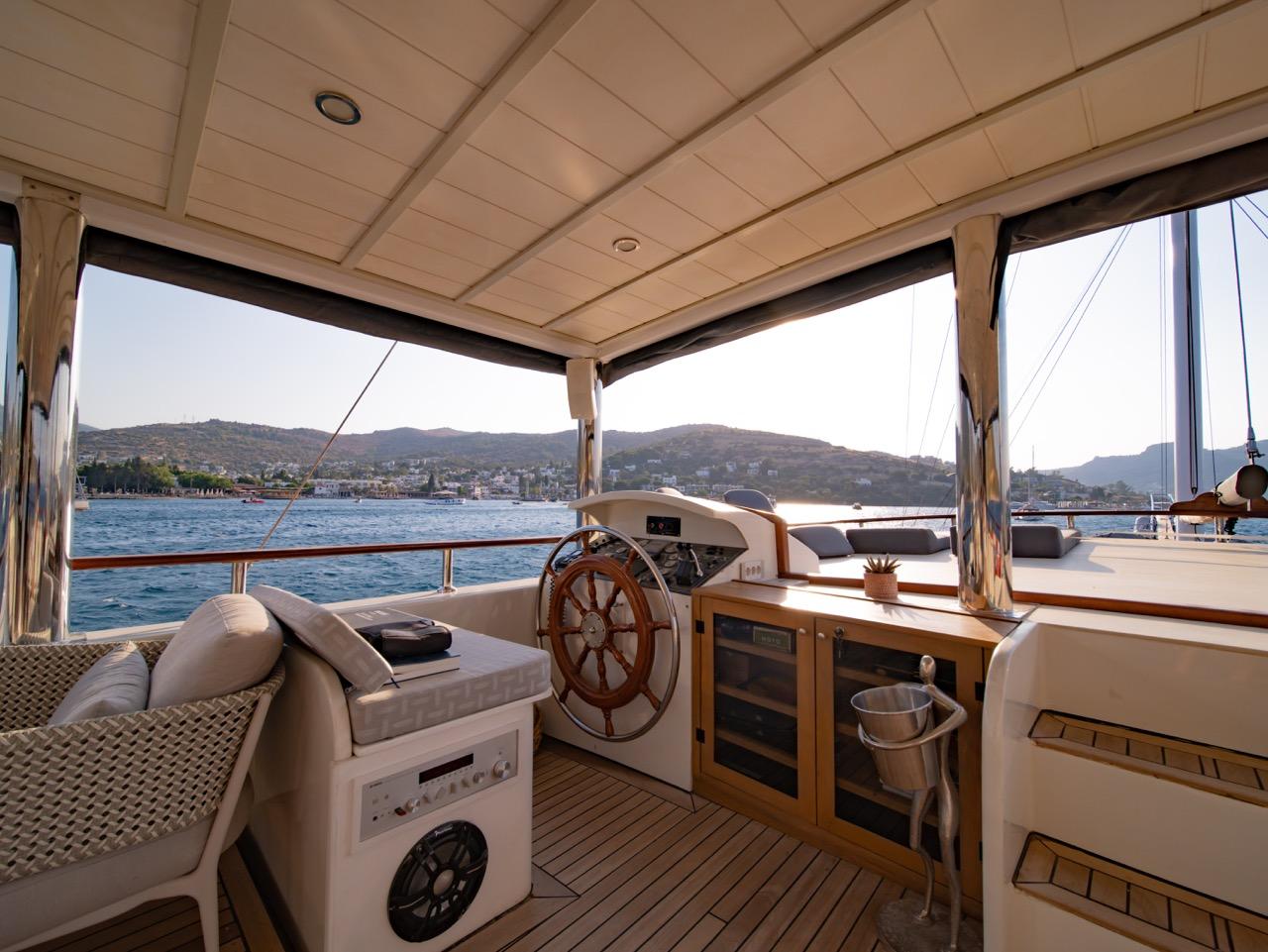 yacht helm station with traditional ship's wheel, covered seating area and coastal mountain views