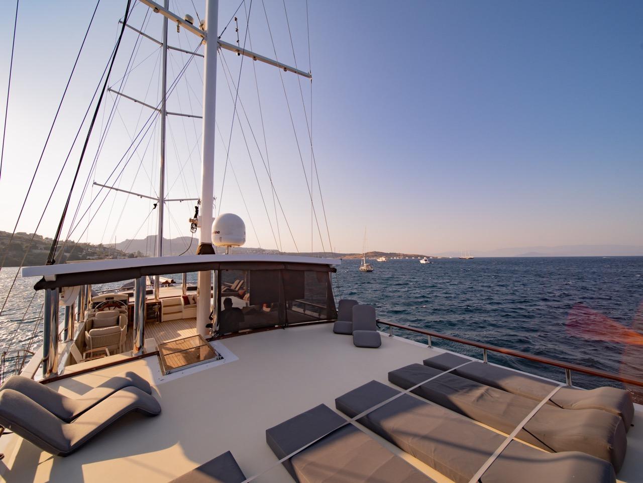 bow deck seating area with grey cushions and mountain coastline views at sunset