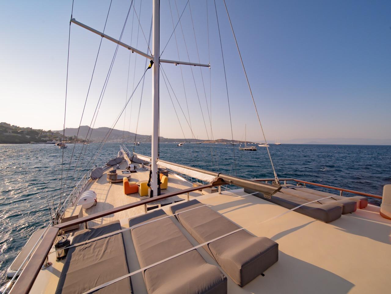 bow deck with beige sun loungers and cushions beneath sailing mast and rigging