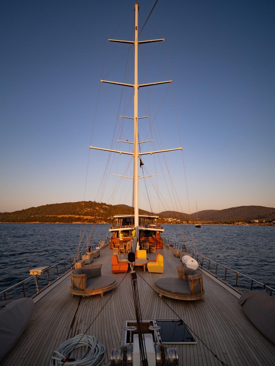 gulet bow deck with outdoor seating furniture and tall sailing mast at sunset