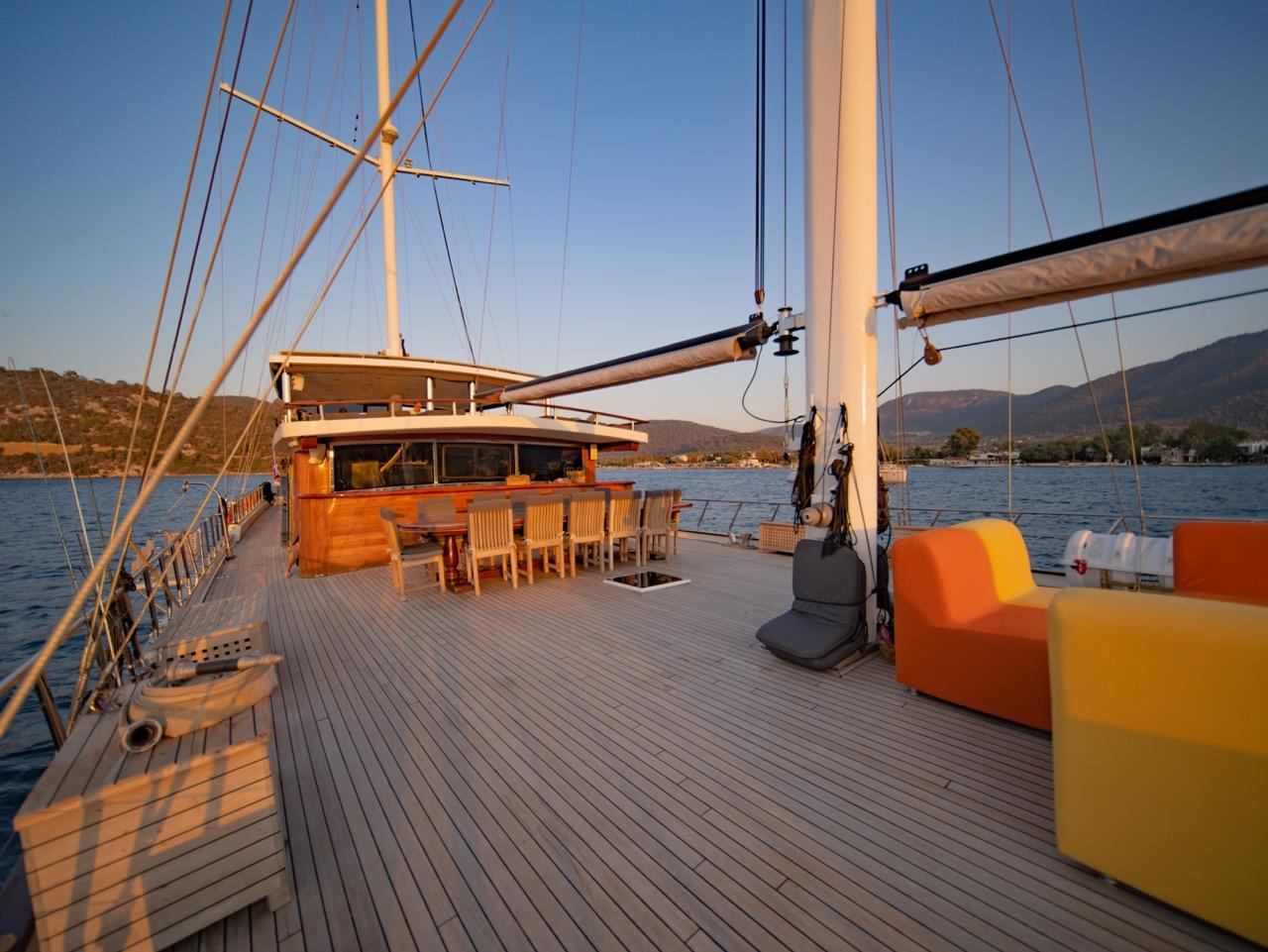 yacht main deck with teak flooring, outdoor dining table and bright orange seating cushions at sunset
