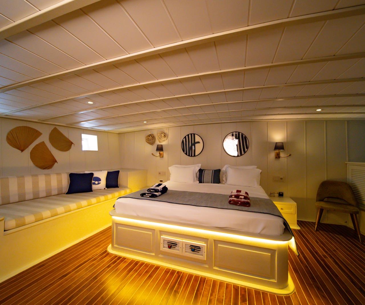 yacht cabin interior with double bed, striped built-in seating, wooden flooring and ambient lighting