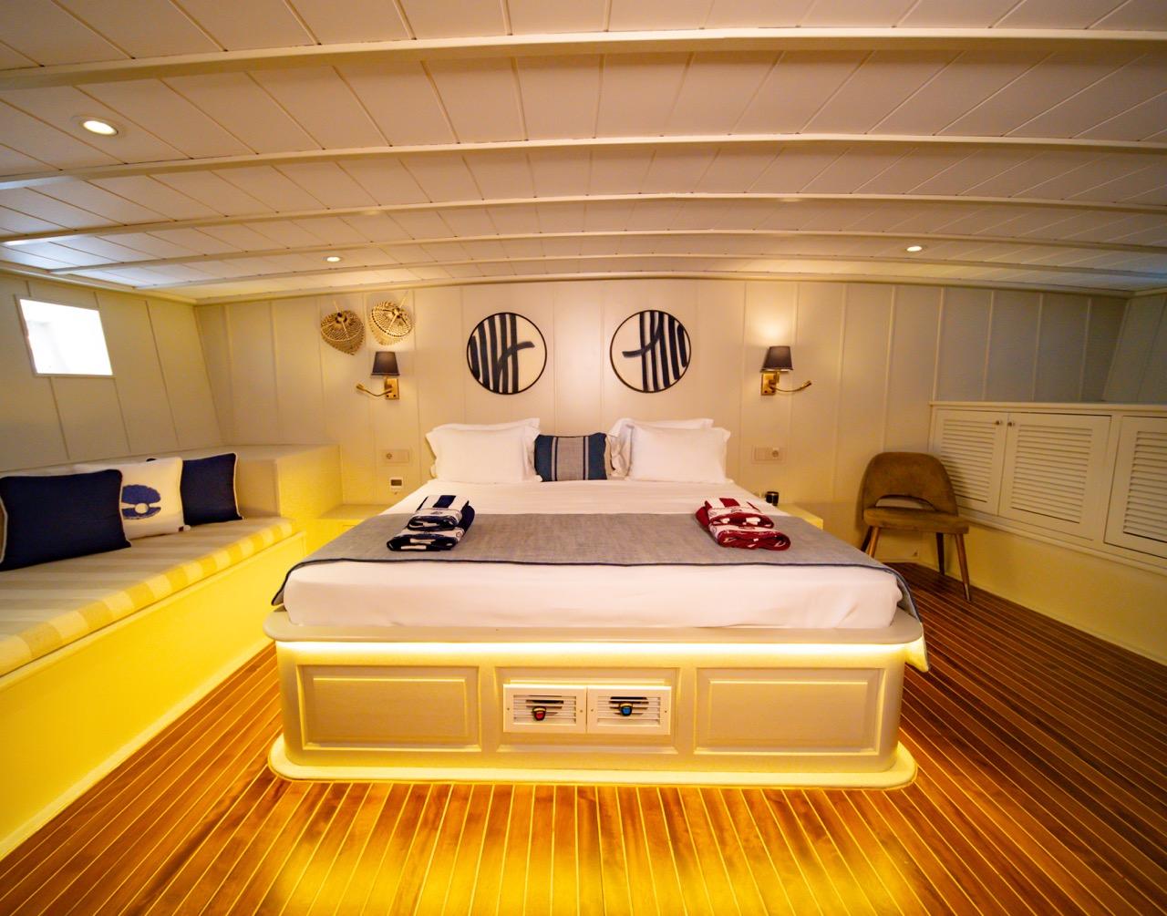 luxury yacht master cabin featuring king bed with white linens, yellow LED lighting, nautical wall art, and teak flooring