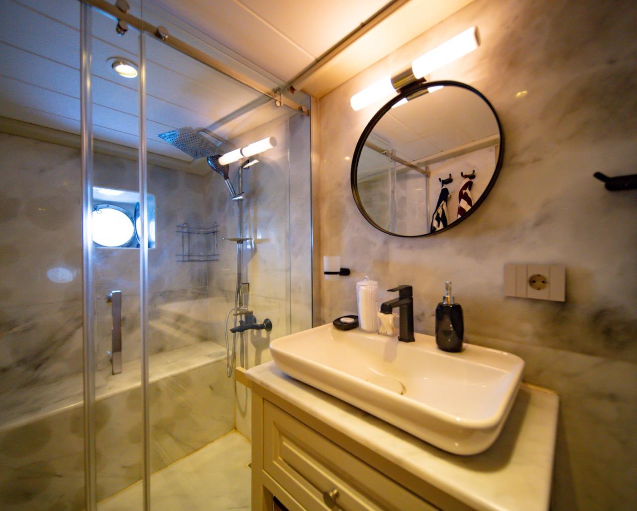 Modern yacht bathroom featuring glass shower enclosure, white basin, and round mirror