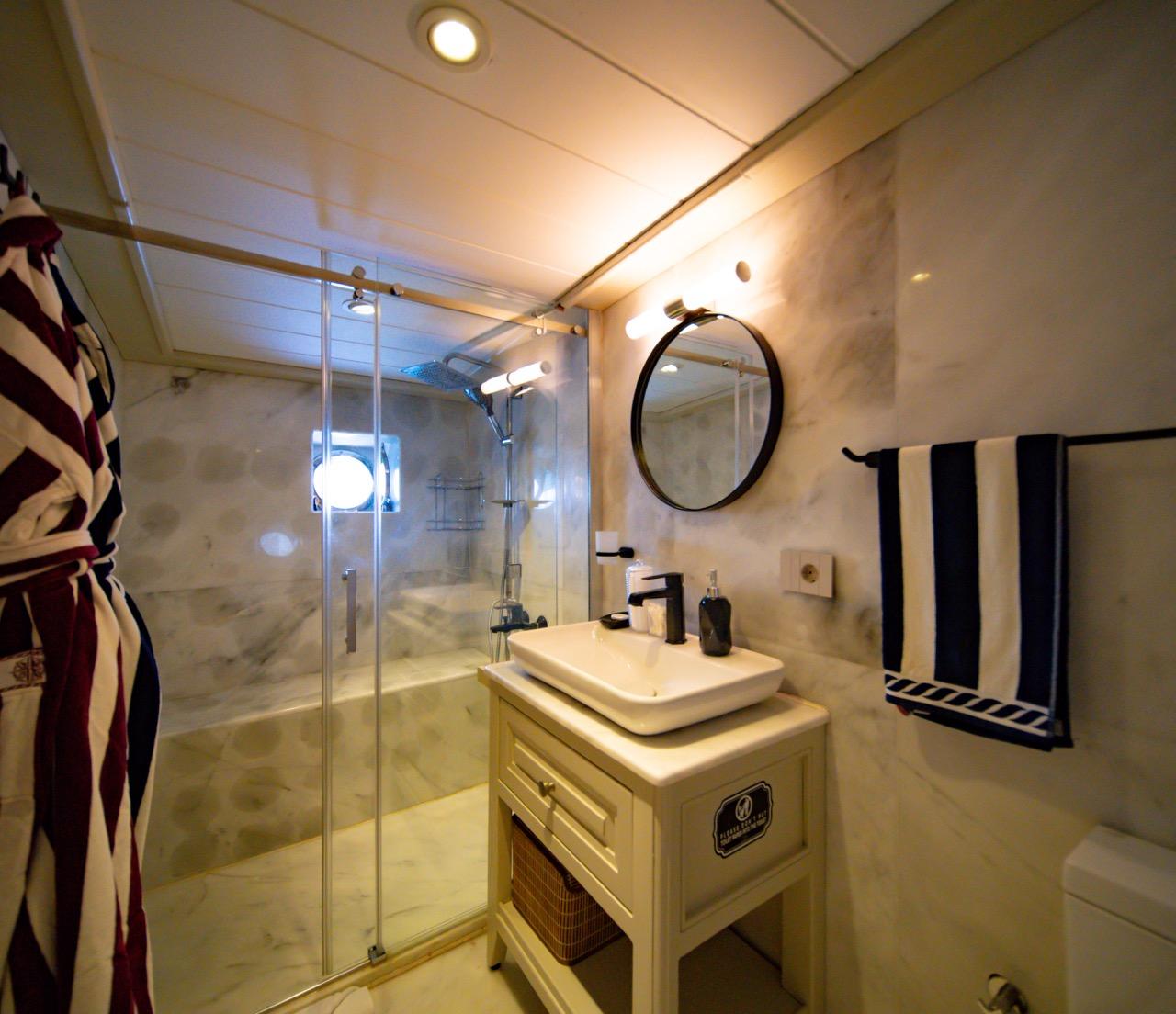 Yacht bathroom featuring marble walls, glass shower enclosure, white vanity with vessel sink