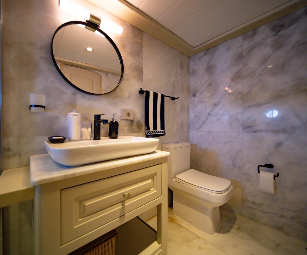 luxury yacht bathroom featuring marble walls, vessel sink on white vanity, and black round mirror