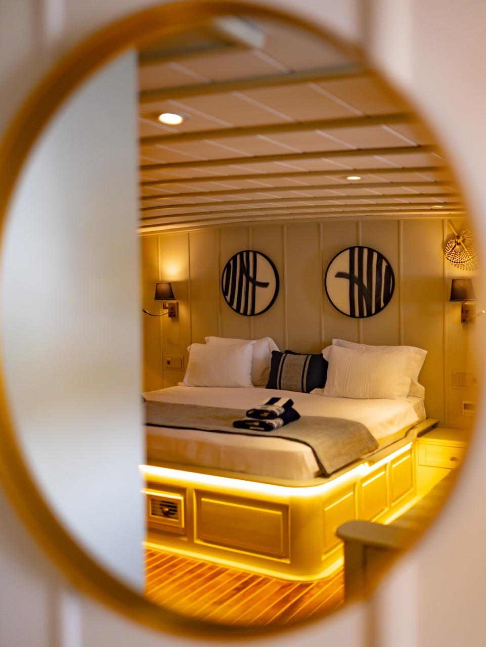 yacht guest cabin featuring double bed with white linens and two circular porthole windows