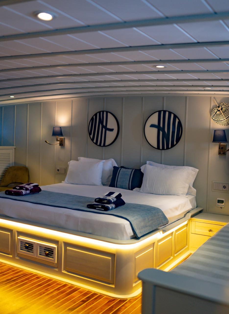 yacht guest cabin featuring double bed with blue striped runner and circular porthole wall art