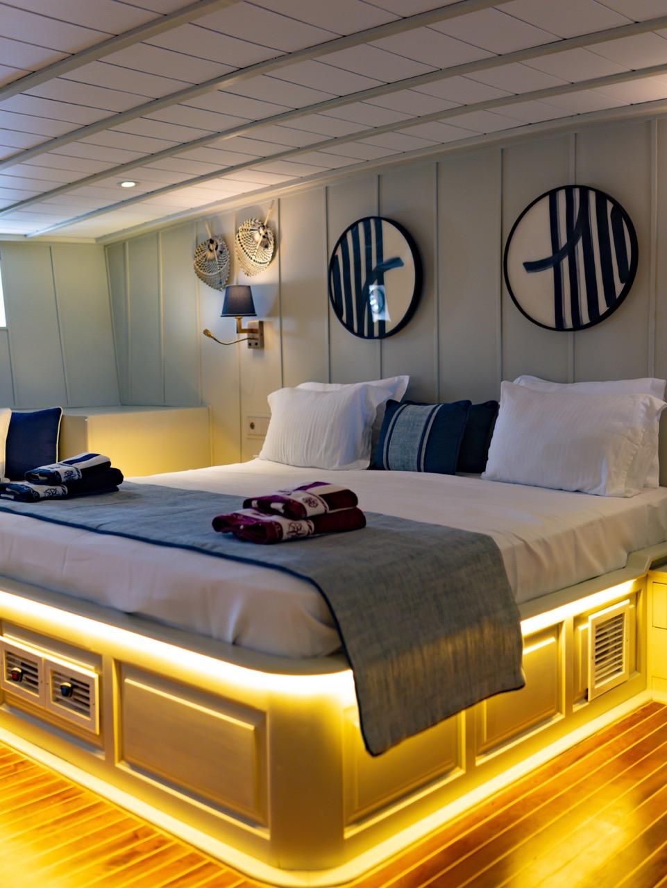 yacht guest cabin with white bedding, built-in storage, wall sconces and under-bed lighting