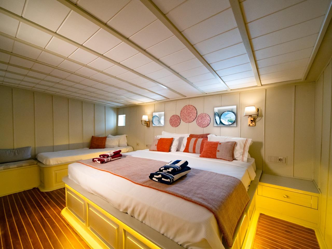 yacht guest cabin featuring twin beds with orange pillows, wood paneling, and round portholes