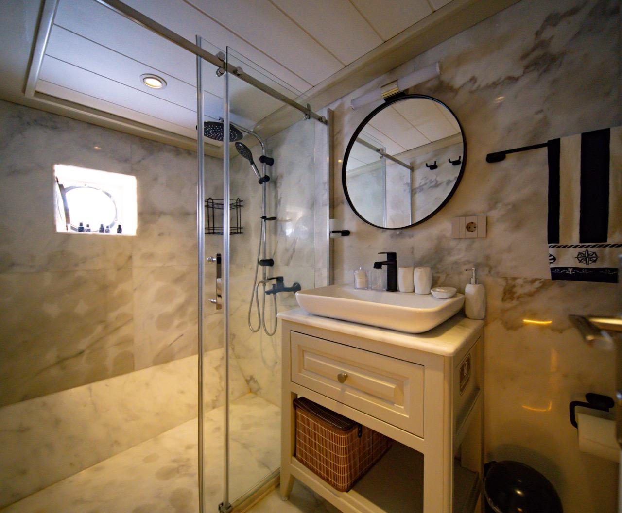 luxury yacht bathroom featuring marble walls, glass shower enclosure, vessel sink and round mirror