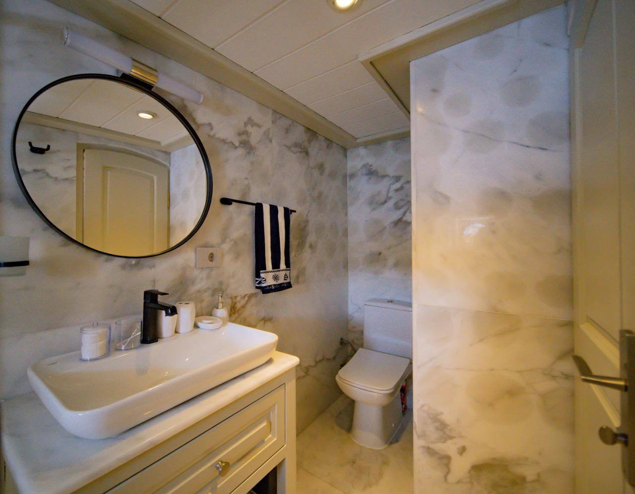 yacht bathroom featuring marble walls, white vanity, round mirror and glass shower enclosure