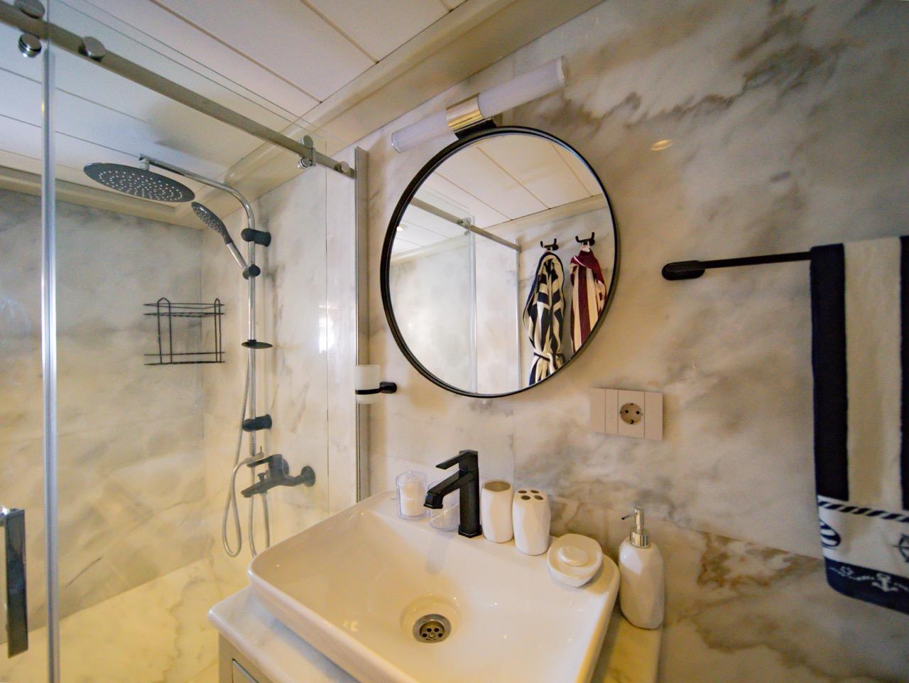 luxury yacht bathroom featuring marble walls, rainfall shower system, round mirror and white basin