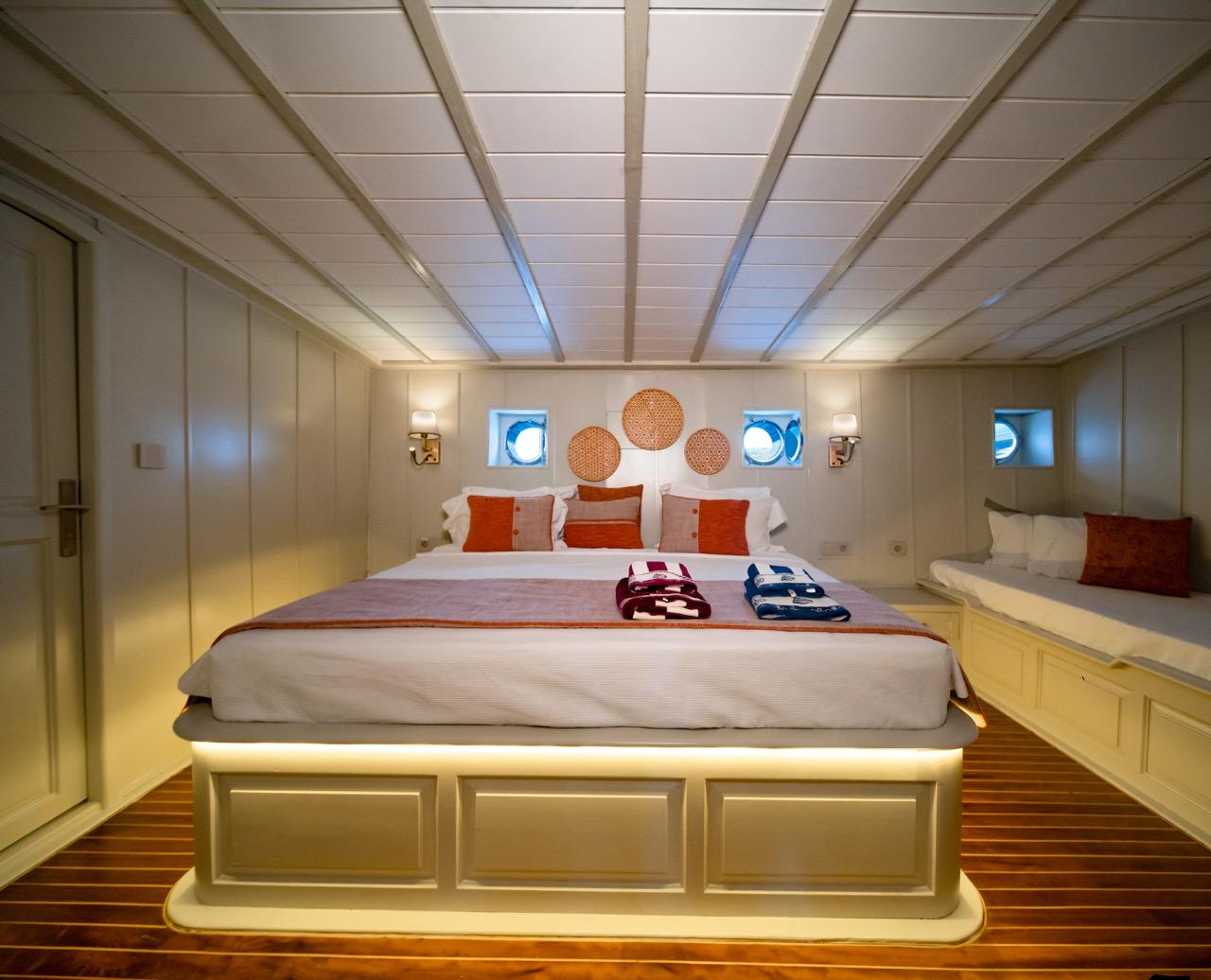 yacht cabin featuring king bed with orange pillows, built-in bench seating, portholes and wooden flooring