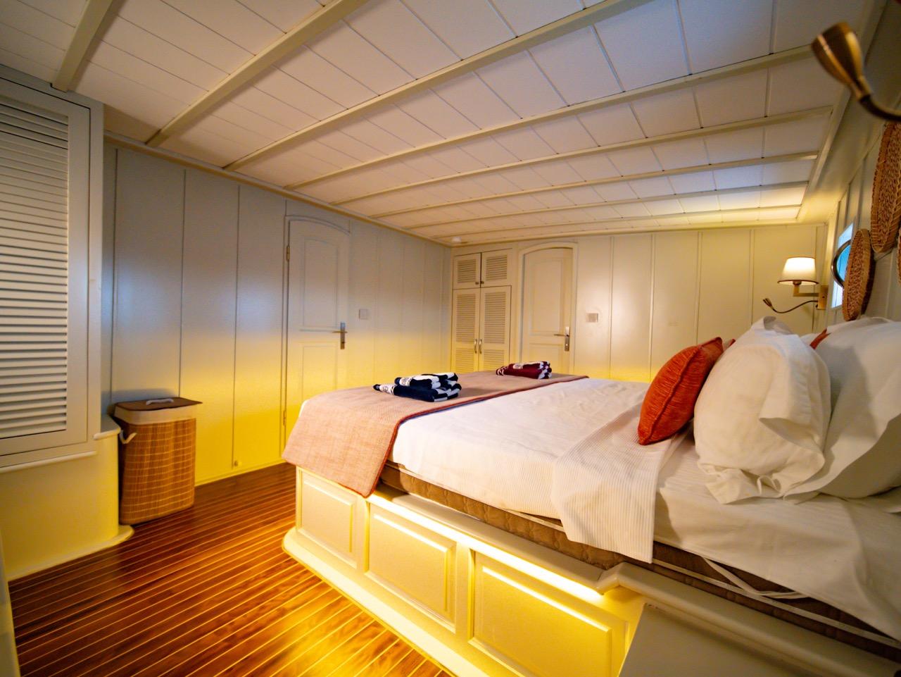 yacht guest cabin featuring double bed with white linens, red accent pillows, wooden flooring and built-in storage