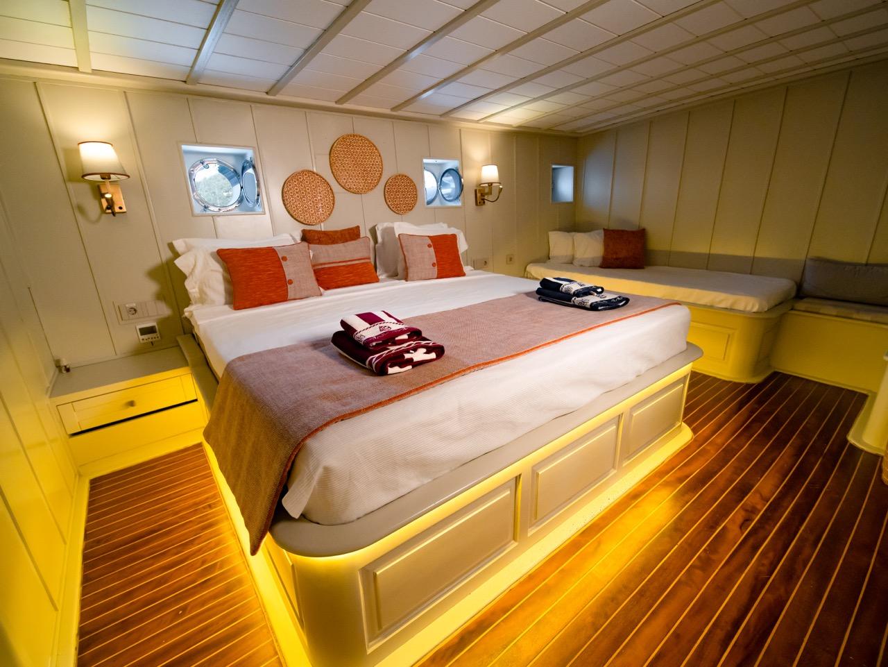 yacht cabin interior with white bed, orange pillows, circular wall art and ambient lighting