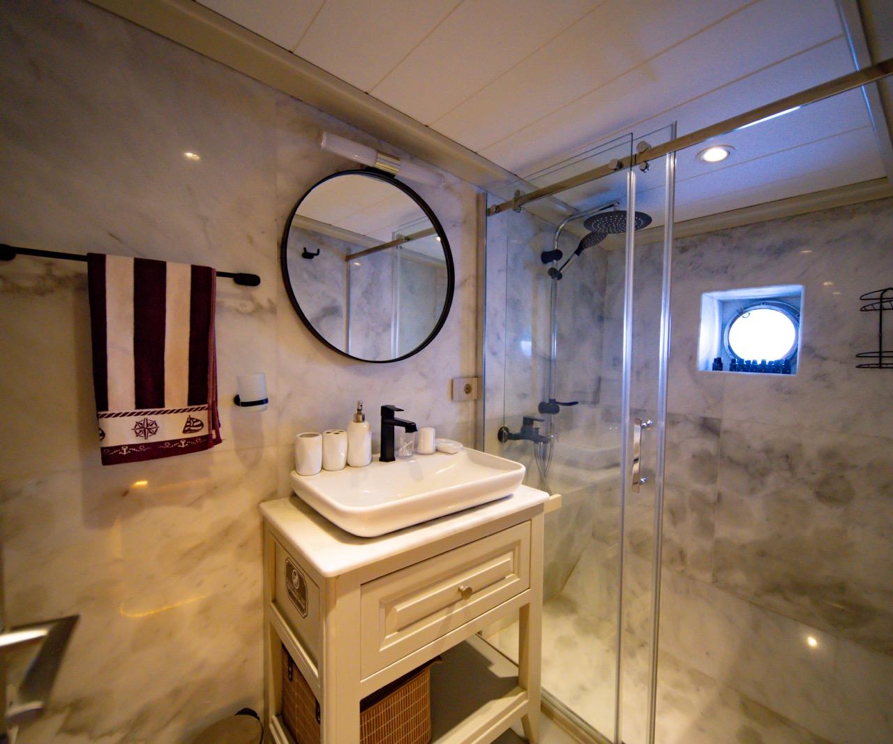 luxury yacht bathroom featuring marble walls, glass shower enclosure, vessel sink and round mirror